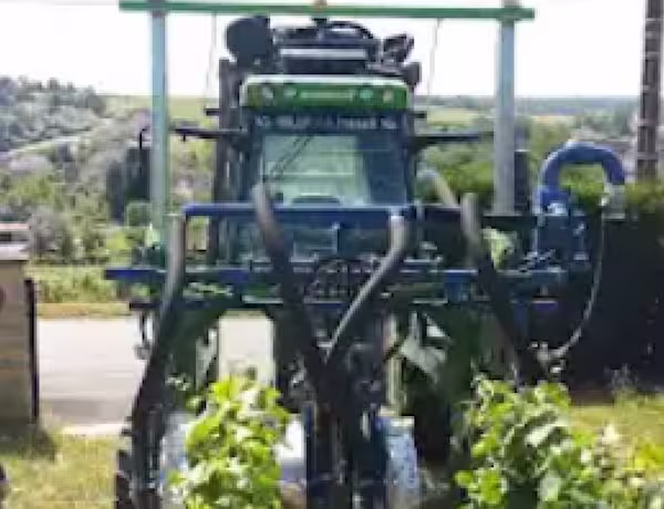 Tracteur agricole équipé de tuyaux, stationné sous une structure près d’un champ.