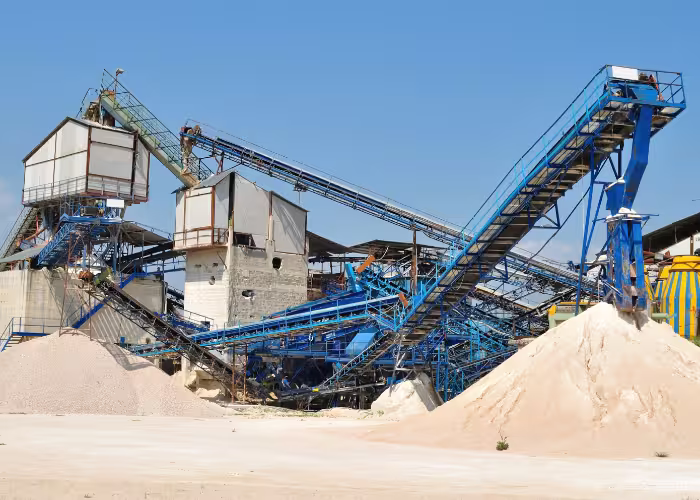 Installation industrielle avec convoyeurs et tas de sable dans une carrière sous ciel dégagé.