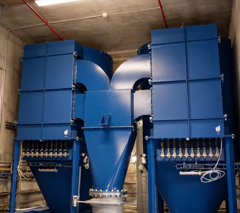 Deux grands dépoussiéreurs bleus avec trémie centrale dans un local technique.