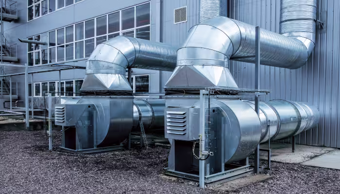 Unités de ventilation extérieures reliées à de larges conduits métalliques le long d’un bâtiment industriel.