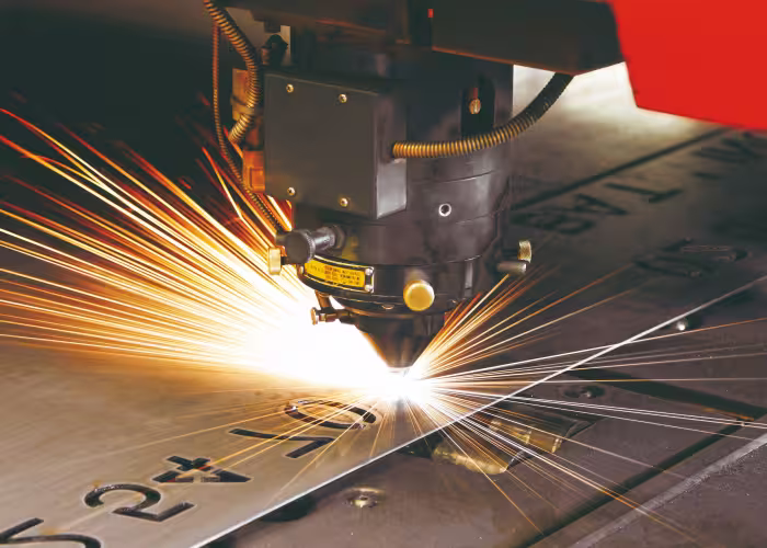 Tête de découpe laser découpant une plaque métallique, étincelles vives jaillissant autour.