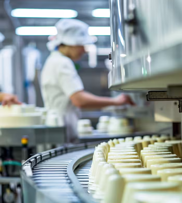 Produits alimentaires sur convoyeur, employé en tenue blanche en arrière-plan.