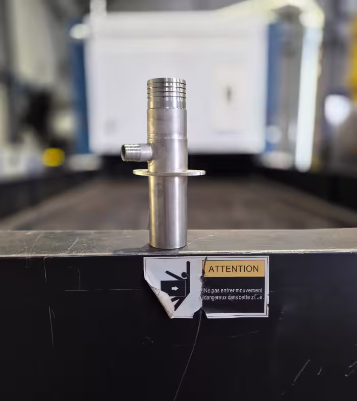 Pièce métallique posée sur une machine, devant une étiquette d’avertissement.