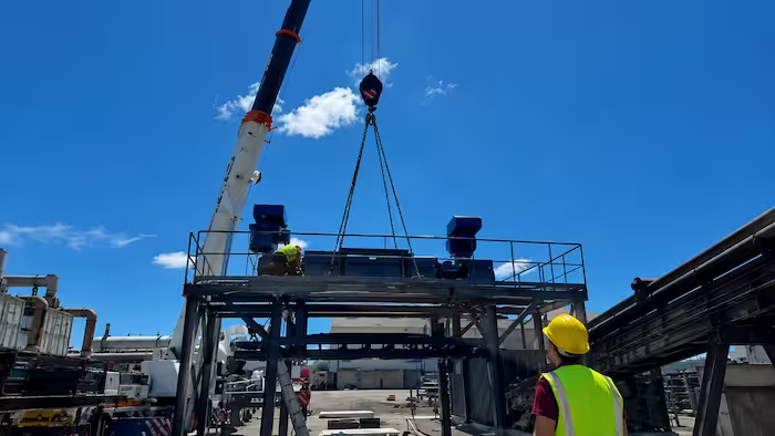 Grue levant un équipement industriel sous la supervision d’ouvriers casqués.